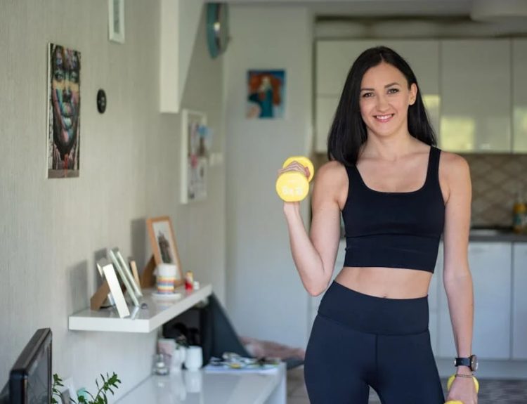 Smiling woman in activewear lifting dumbbells at home for a healthy lifestyle.